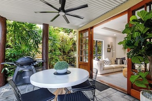 A patio with a round table, chairs, a grill, and a ceiling fan.