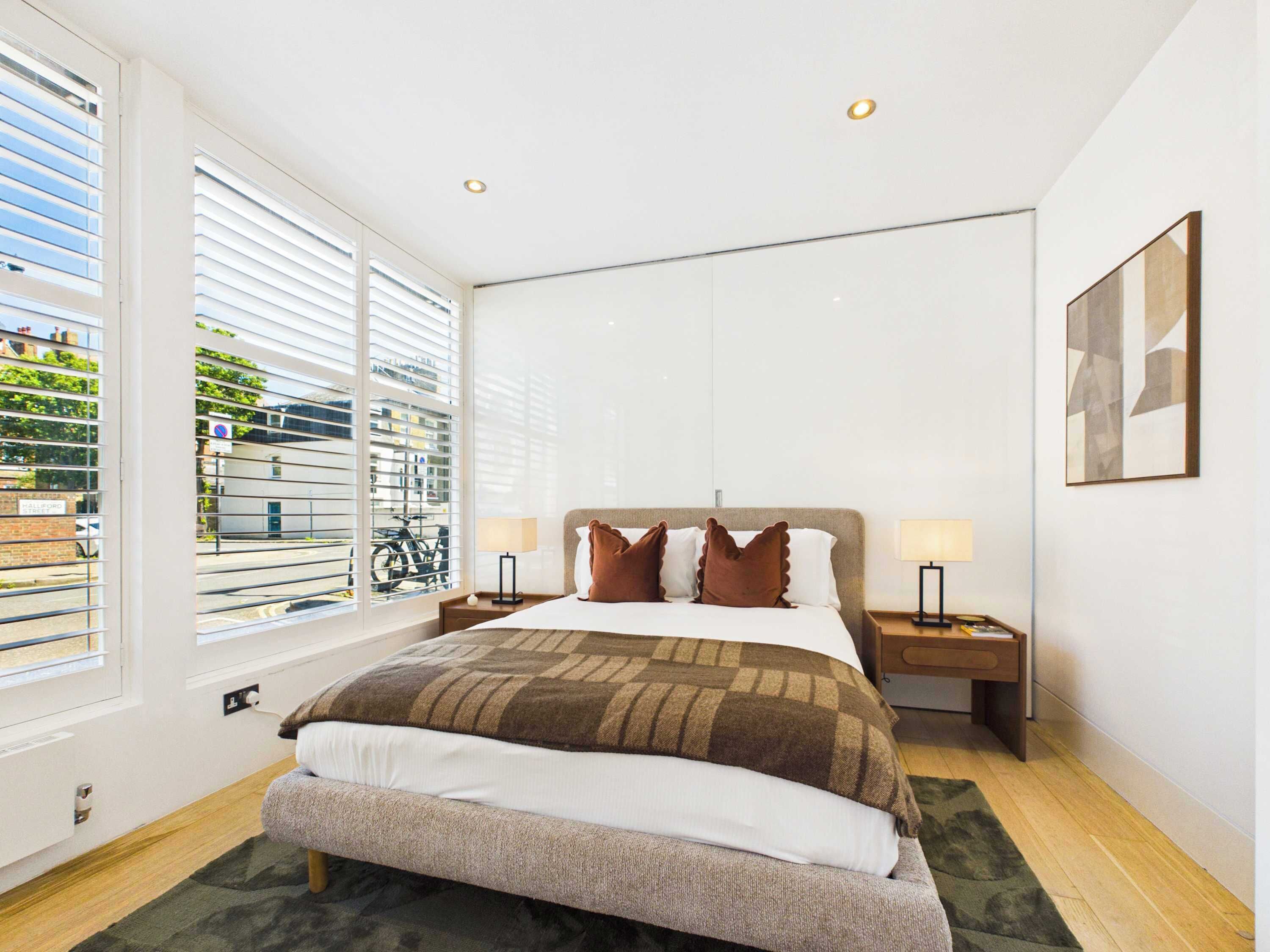 Une chambre d’hôtel moderne, dotée d’un grand lit, de deux tables de chevet, d’une fenêtre avec stores et offrant une vue sur l’extérieur.
