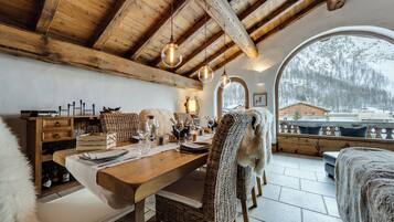 A wooden dining table with chairs, a bench, and a view of a snowy landscape through a large arched window.