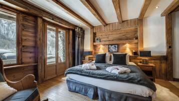 A wooden cabin bedroom with a large bed, a rocking chair, and a stone wall.