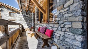 A wooden deck with a stone wall, wooden beams, a bench, and a window with a view.