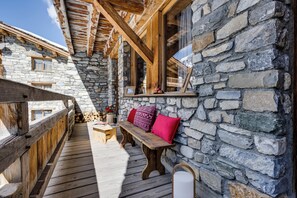 A wooden deck with a stone wall, wooden beams, a bench, and a window with a view. - Chalet La Bouclia - Luxury Alpine retreat (Val-d'Isère)