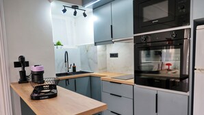 A modern kitchen with a wooden table, grey cabinets, a black oven, and a microwave. - In the heart of Nafpaktos's city center, 50m from the sea and 5' from the port. (Nafpaktos)