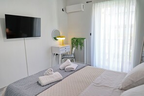 A hotel room with a bed, a TV, a bedside lamp, a mirror, a radiator, and a window with curtains. - In the heart of Nafpaktos's city center, 50m from the sea and 5' from the port. (Nafpaktos)