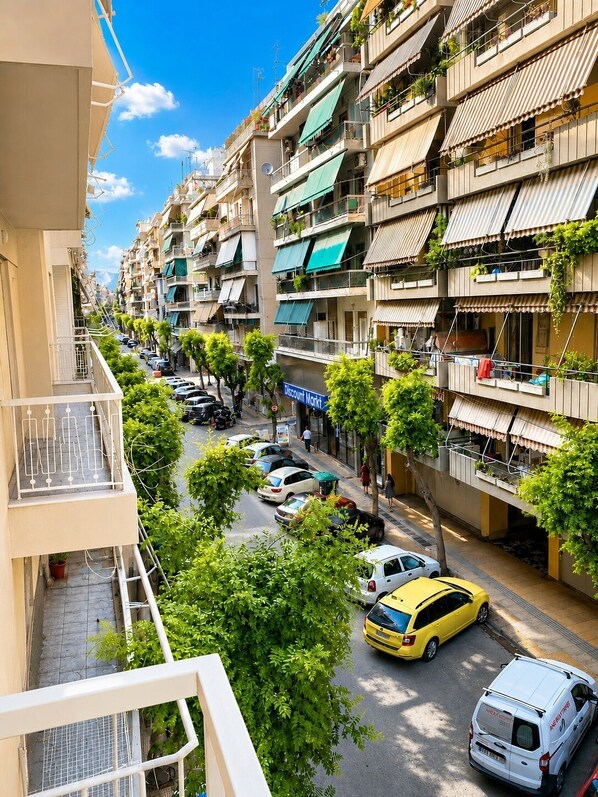 Un immeuble résidentiel à plusieurs étages, doté de balcons, donnant sur la rue, avec des voitures garées et un ciel dégagé.