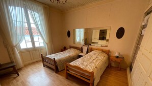 Ett rum med två sängar i trä, en spegel, ett litet bord och ett fönster med gardiner.