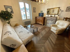 Ein Wohnzimmer mit einer Couch, einem Sessel, Holzboden im Fischgrätmuster, einem Fernseher und einem Kamin.