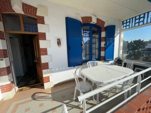 Ein Zimmer mit weißem Tisch und Stühlen, einem Fenster mit blauen Rolläden und einer Tür zu einem anderen Raum.