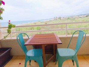 A balcony with a wooden table and two chairs, overlooking a beach and distant buildings. - Beachfront Apartment with Sea-View Terrace (Calafell)
