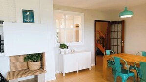 A modern kitchen with white cabinetry, a wooden dining table, teal chairs, and a hanging light fixture. - Beachfront Apartment with Sea-View Terrace (Calafell)
