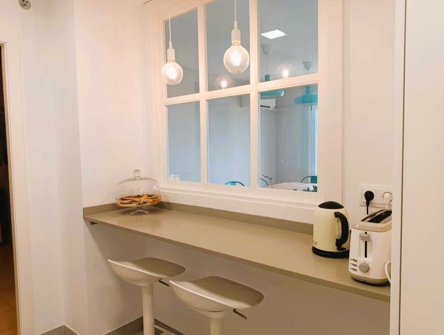 Une cuisine avec une fenêtre, deux lampes suspendues, un garde-pain et une machine à café.