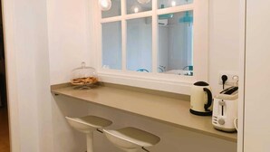 A kitchen with a window, two hanging light bulbs, a bread box, and a coffee maker. - Beachfront Apartment with Sea-View Terrace (Calafell)