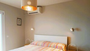 A bedroom with a bed, an air conditioning unit, a chair, and a wall-mounted light fixture. - Beachfront Apartment with Sea-View Terrace (Calafell)