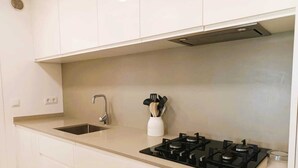A modern kitchen with a sink, stove, and utensil holder. - Beachfront Apartment with Sea-View Terrace (Calafell)