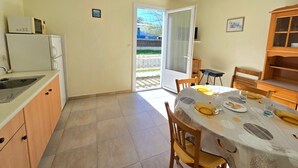 Eine kompakte Küche mit Spüle, Mikrowelle und Schränken, ein Essbereich mit Tisch für zwei Personen und eine Glastür zum Balkon.