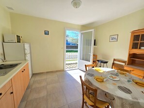 Eine kompakte Küche mit Spüle, Mikrowelle und Schränken, ein Essbereich mit Tisch für zwei Personen und eine Glastür zum Balkon.