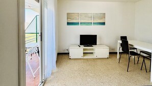 Une pièce équipée d’un téléviseur, d’un bureau et de chaises, d’une porte-fenêtre coulissante donnant sur l’extérieur et d’un tableau accroché au mur.