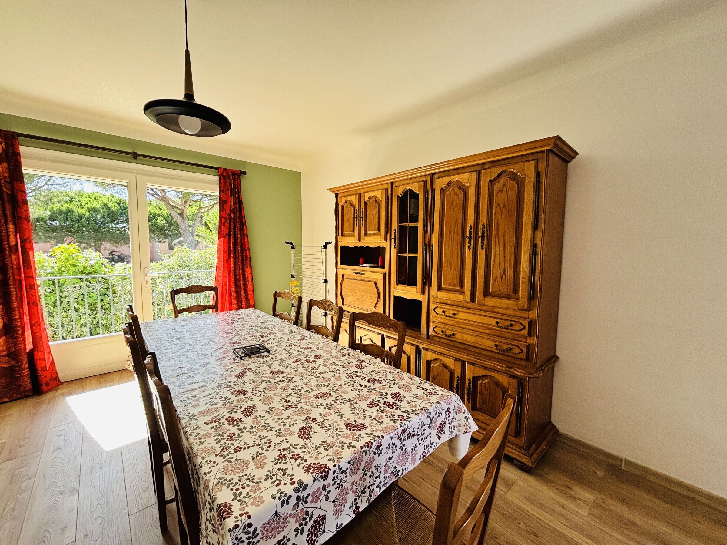 Ein Essbereich mit Tisch, Stühlen, einem Holzschrank und einem Fenster mit Vorhängen.