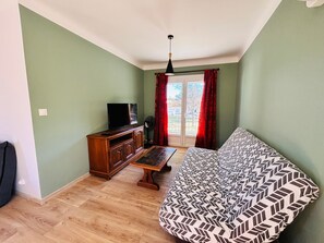 Ein Zimmer mit einer Couch, einem Fernseher auf einem Holzkasten, einem Ventilator und einer Tür, die nach draußen führt.