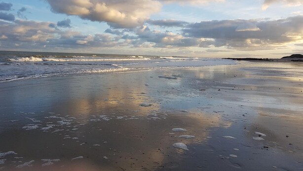 Une plage avec des vagues, un ciel nuageux et une colline lointaine.