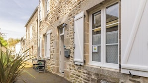 Un bâtiment en pierre avec une porte, des fenêtres et une petite table entourée de chaises à l’extérieur.