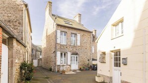 Une rue étroite bordée d’immeubles en pierre, avec une porte centrale et des plantes en pot.