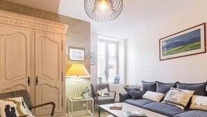 Un salon avec un canapé, un fauteuil, une lampe et une grande fenêtre.