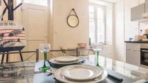 Un coin repas avec une table en verre pour deux personnes, un miroir fixé au mur et une vue sur la cuisine.