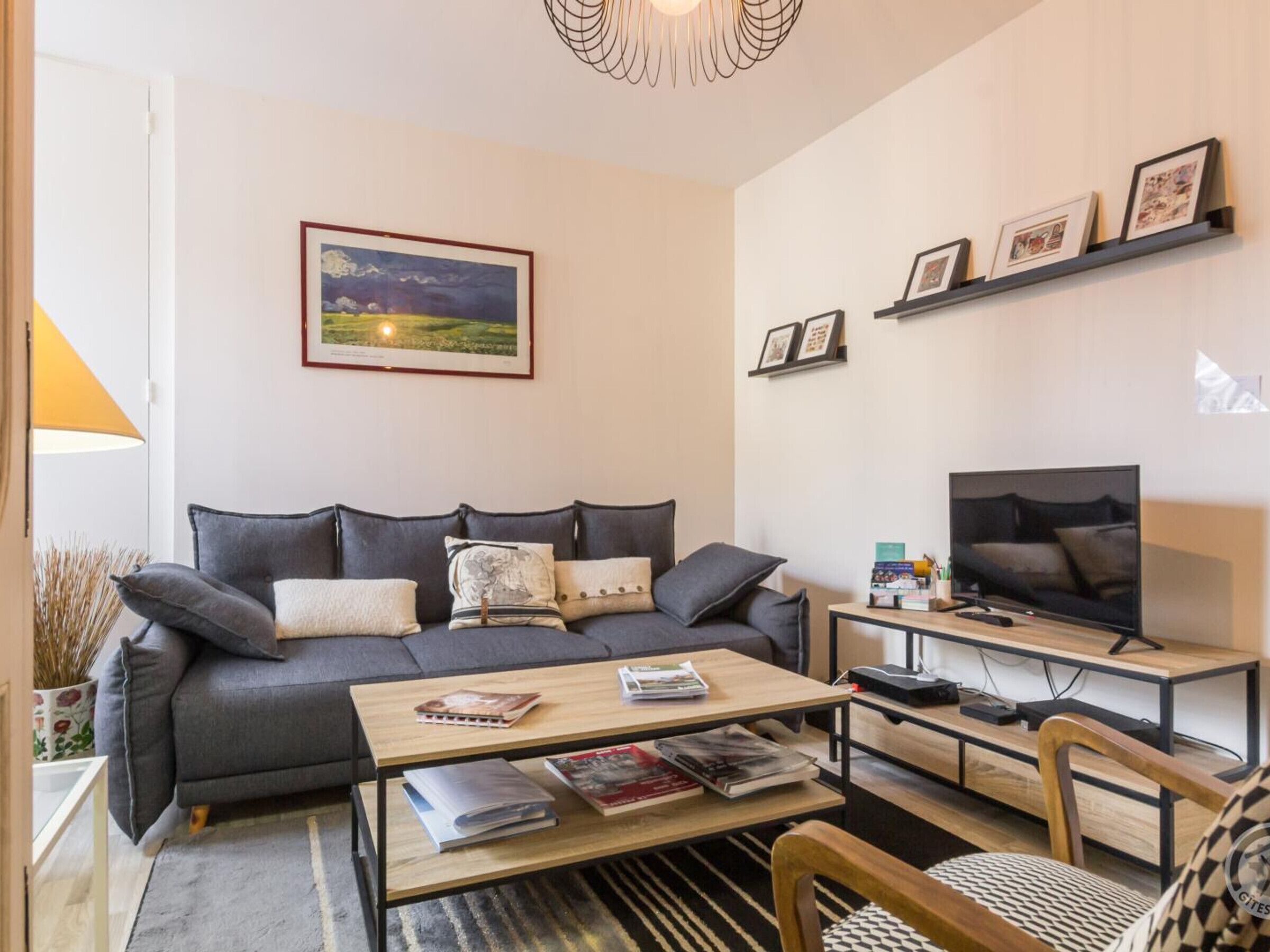 Uma sala de estar com sofá, mesa de centro, TV e quadros nas paredes.