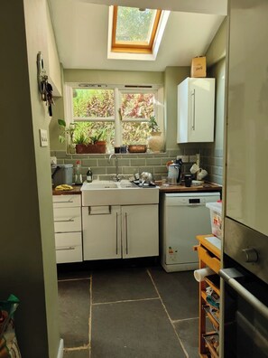 Eine kompakte Küche mit Oberlicht, weißen Schränken, einem Geschirrspüler und einem kleinen Kühlschrank.