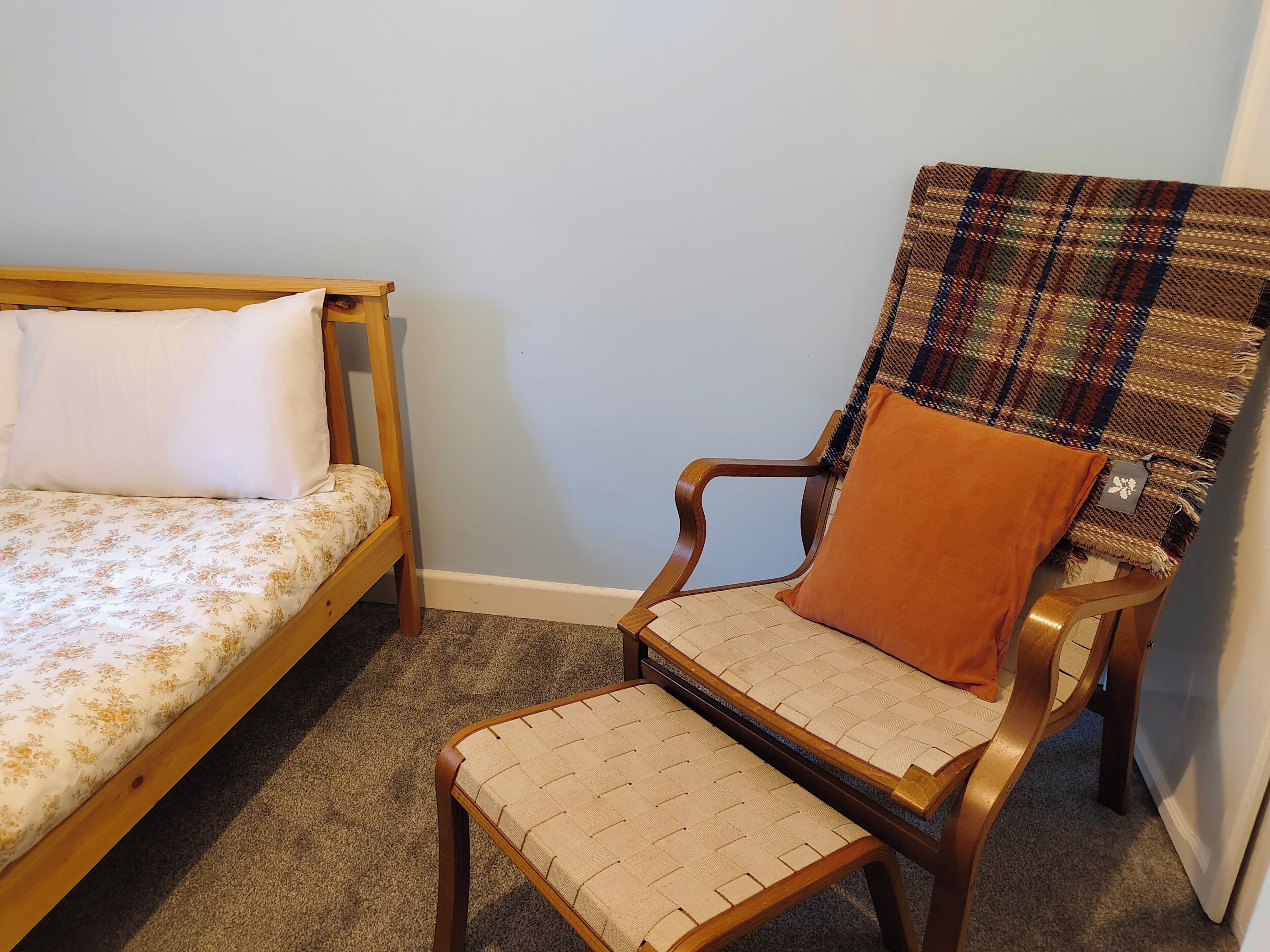Ein Schlafzimmer mit einem hölzernen Bett, einem Stuhl mit Sitzfläche aus Bändern und einer karierten Decke.
