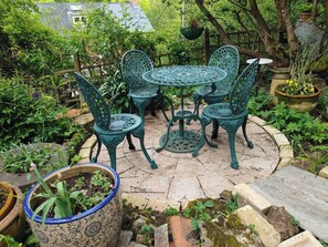 Ein Garten-Terrasse mit einem runden Tisch und vier Stühlen, umgeben von Topfpflanzen und einem Holzzaun.