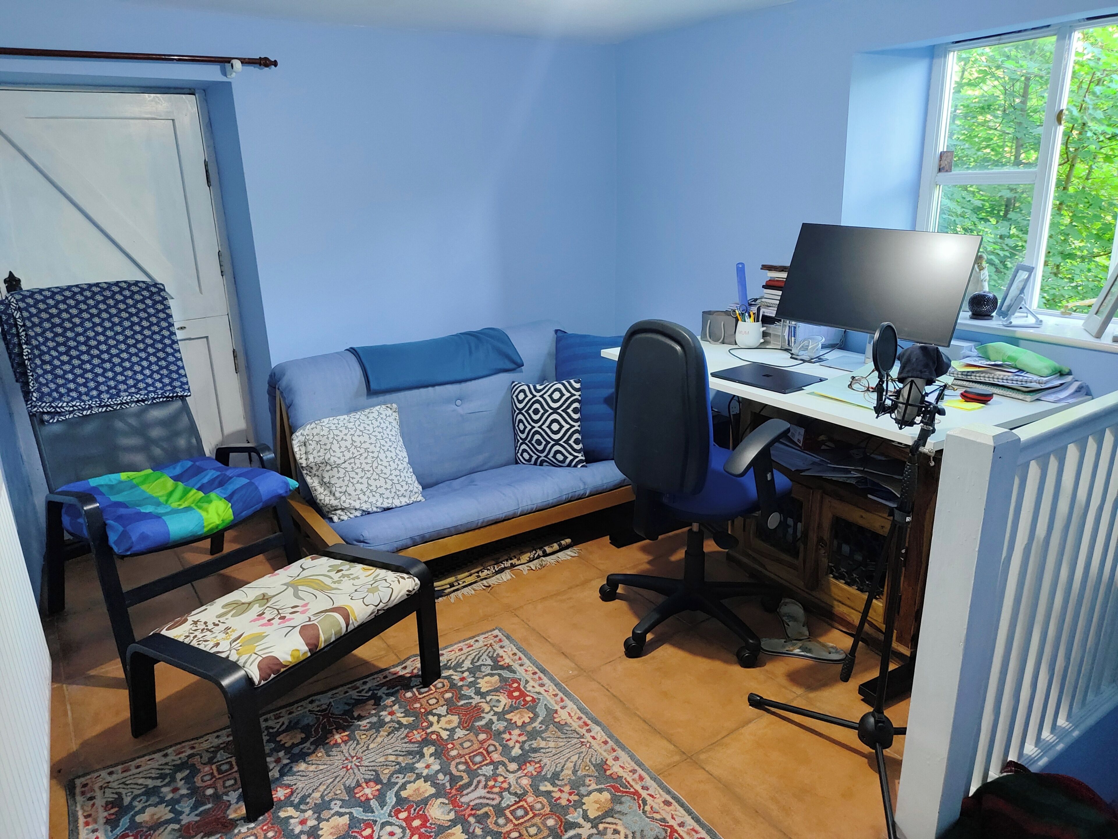 Une pièce comprenant un canapé, un fauteuil, un bureau avec un ordinateur et une fenêtre.