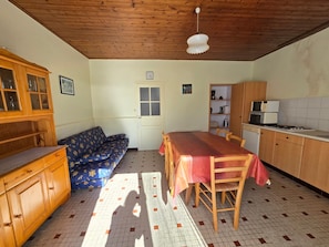 Ein Zimmer mit Holzboden, einem Esstisch mit Stühlen, einer Couch, einem Schrank, einer Mikrowelle und einem Fliesenboden.