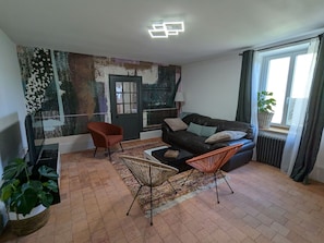A living room with a sofa, two chairs, a coffee table, a patterned rug, a wall with abstract art, a door, and a window with curtains. - Country house, pets welcome - 6 guests (Tavers)