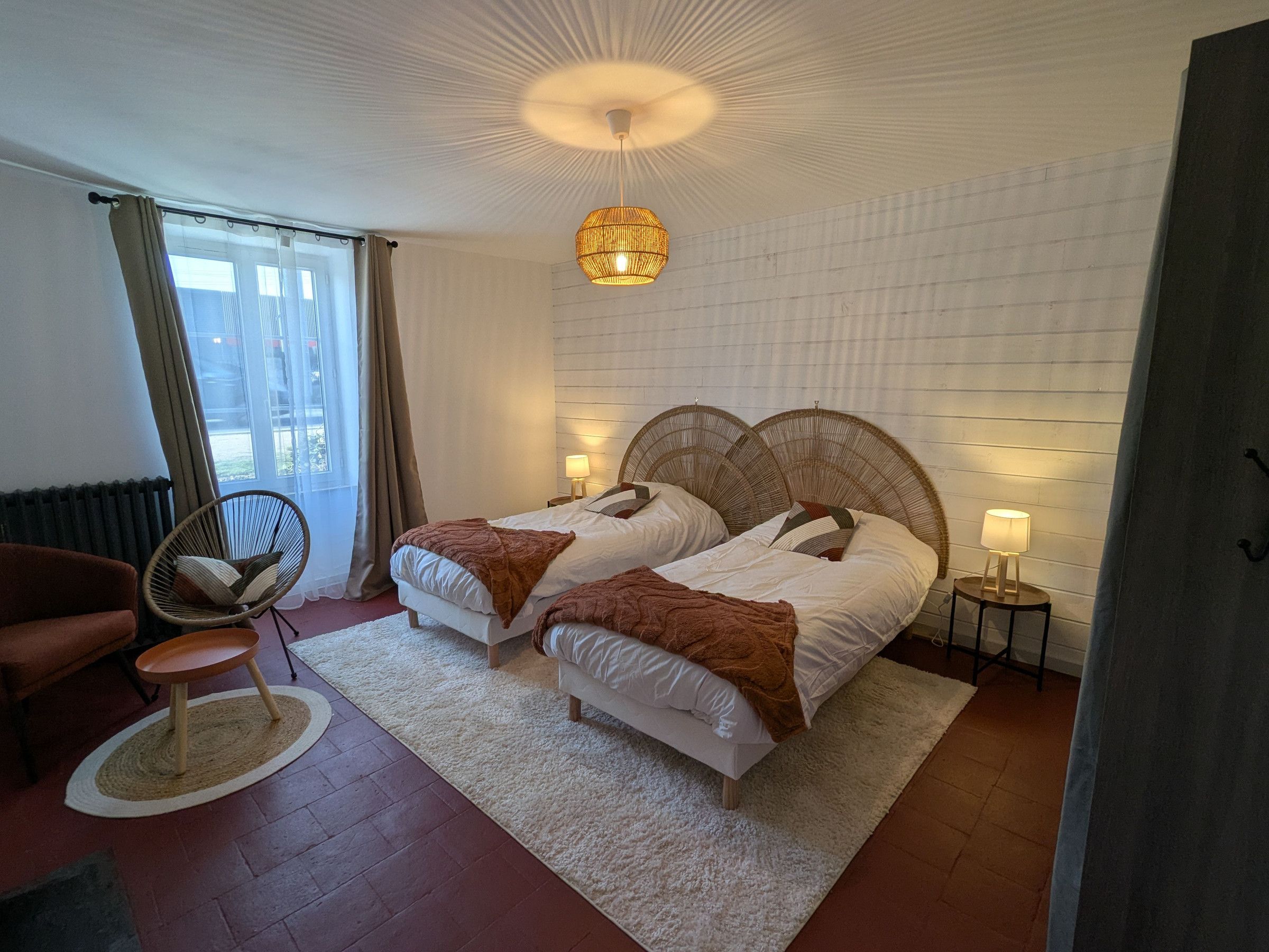 A bedroom with two beds, a chair, a lamp, and a view of the outdoors.