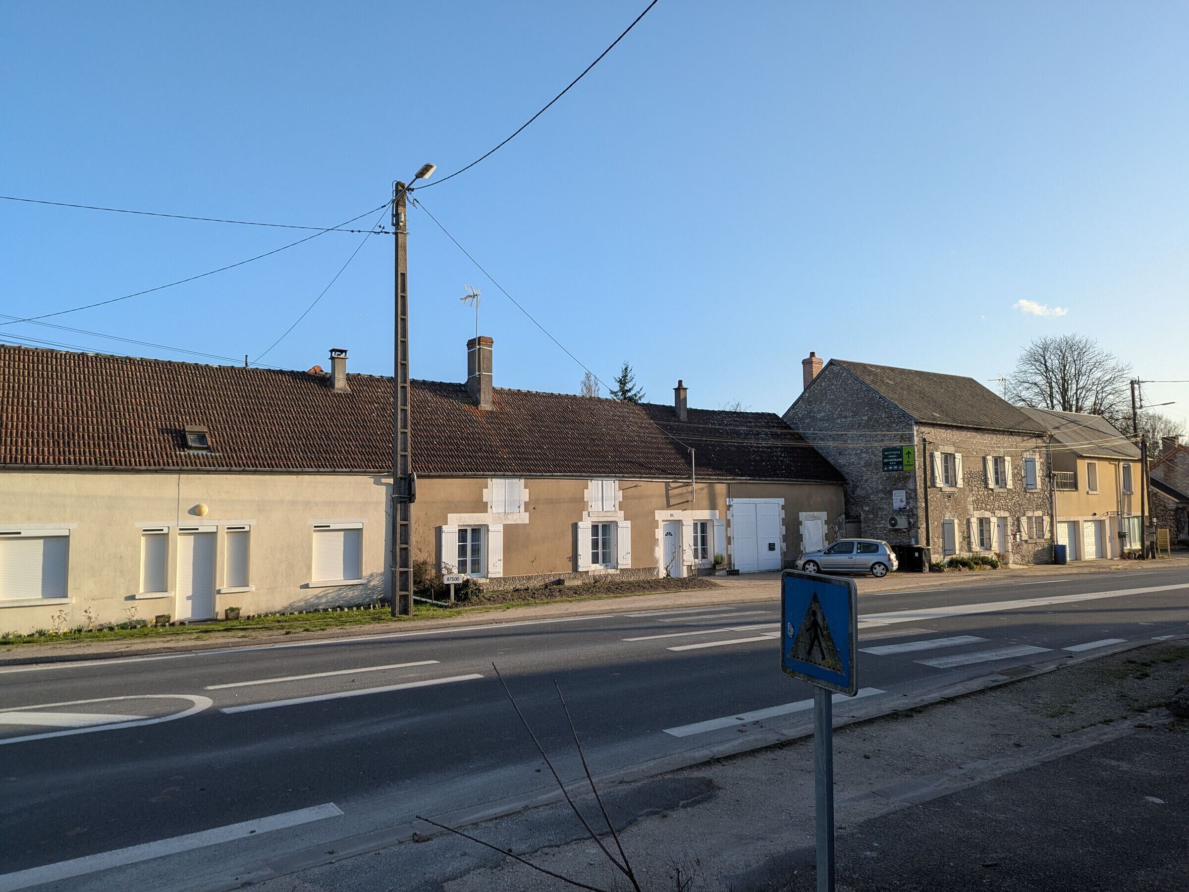 Une rue bordée d’immeubles, un panneau indiquant un passage piéton et une voiture.