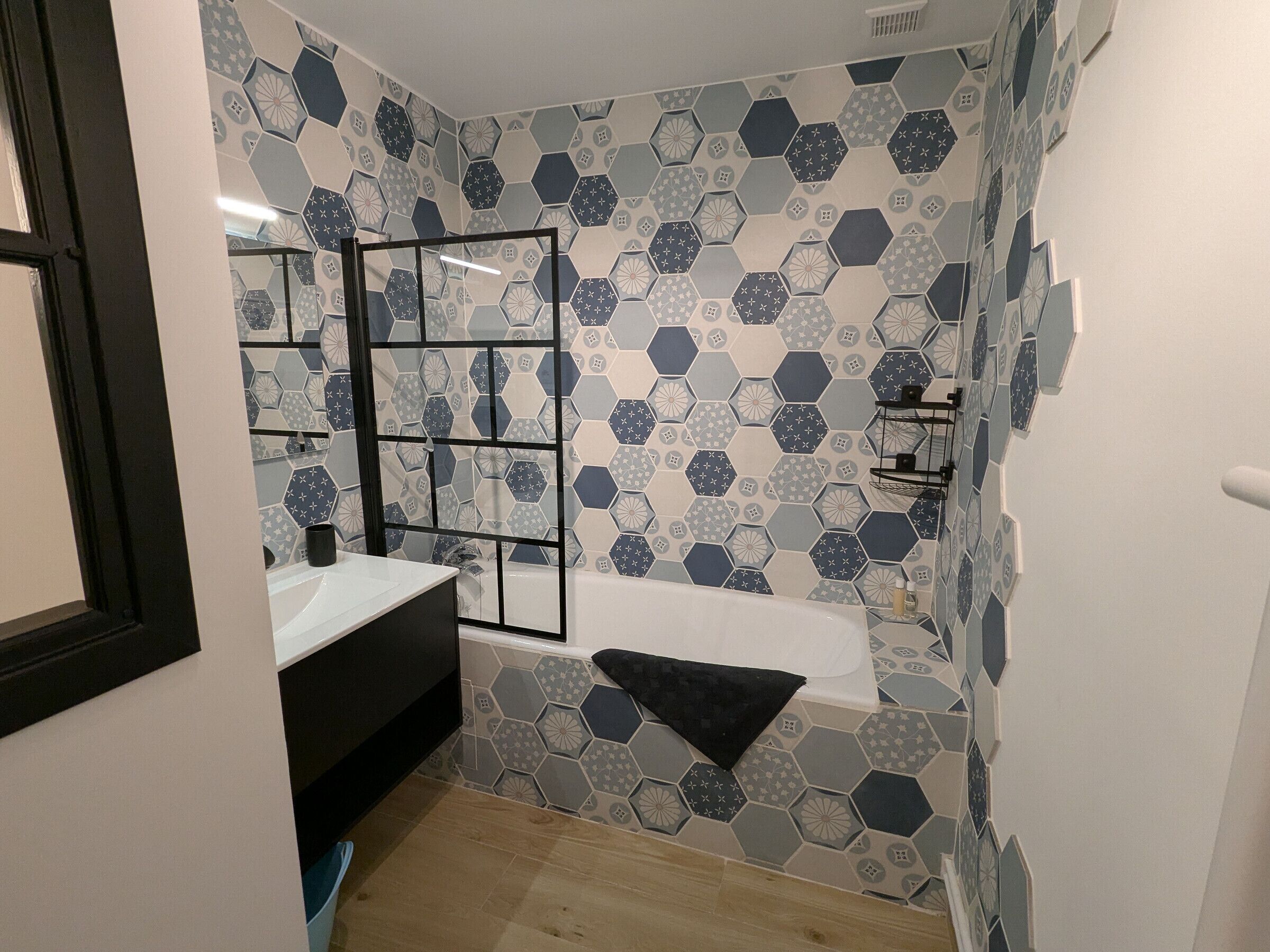 A bathroom with a hexagonal tile pattern, a black-framed mirror, a white sink, and a bathtub.