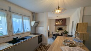 Moderni keittiö, jossa on sisäänrakennettu uuni, ruokailutila puupöydällä sekä takka.