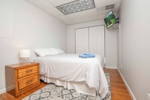 Quarto com cama, mesa de cabeceira, televisão de tela plana e guarda-roupa.
