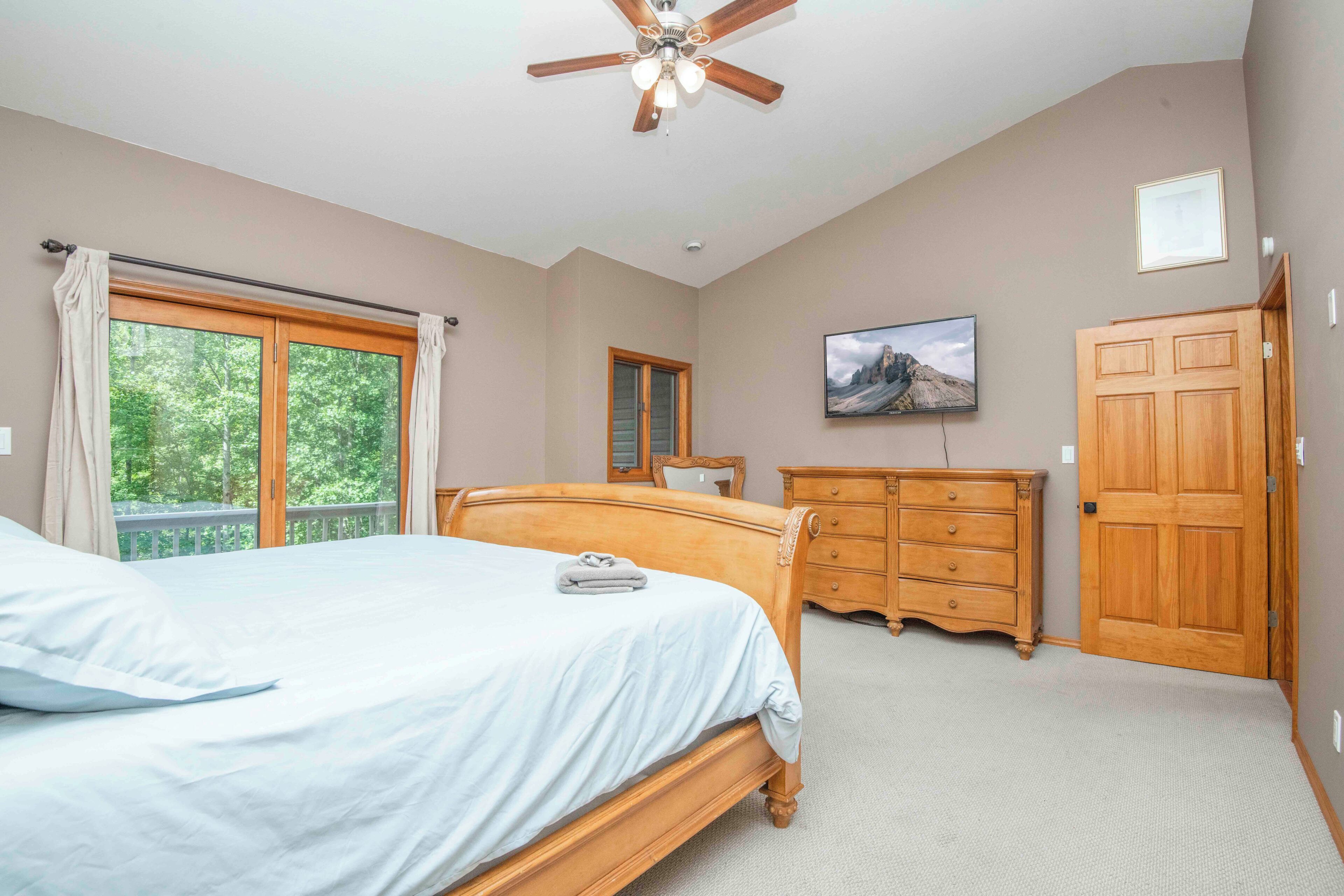 A bedroom with a bed, a dresser, a wardrobe, a ceiling fan, and a window with curtains.