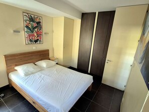 Ein Schlafzimmer mit einem hölzernen Bett, einem Nachttisch, einem Gemälde und einem Kleiderschrank.