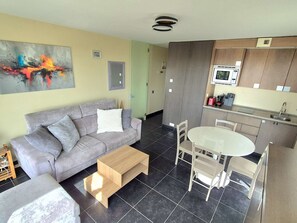 Ein modernes Wohnzimmer mit grauem Sofa, einem Couchtisch und einem Essbereich mit weißem Tisch und Stühlen.