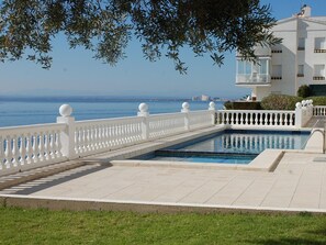 Een zwembad met een witte balustrade, een helder uitzicht op de zee en een gebouw met balkons.