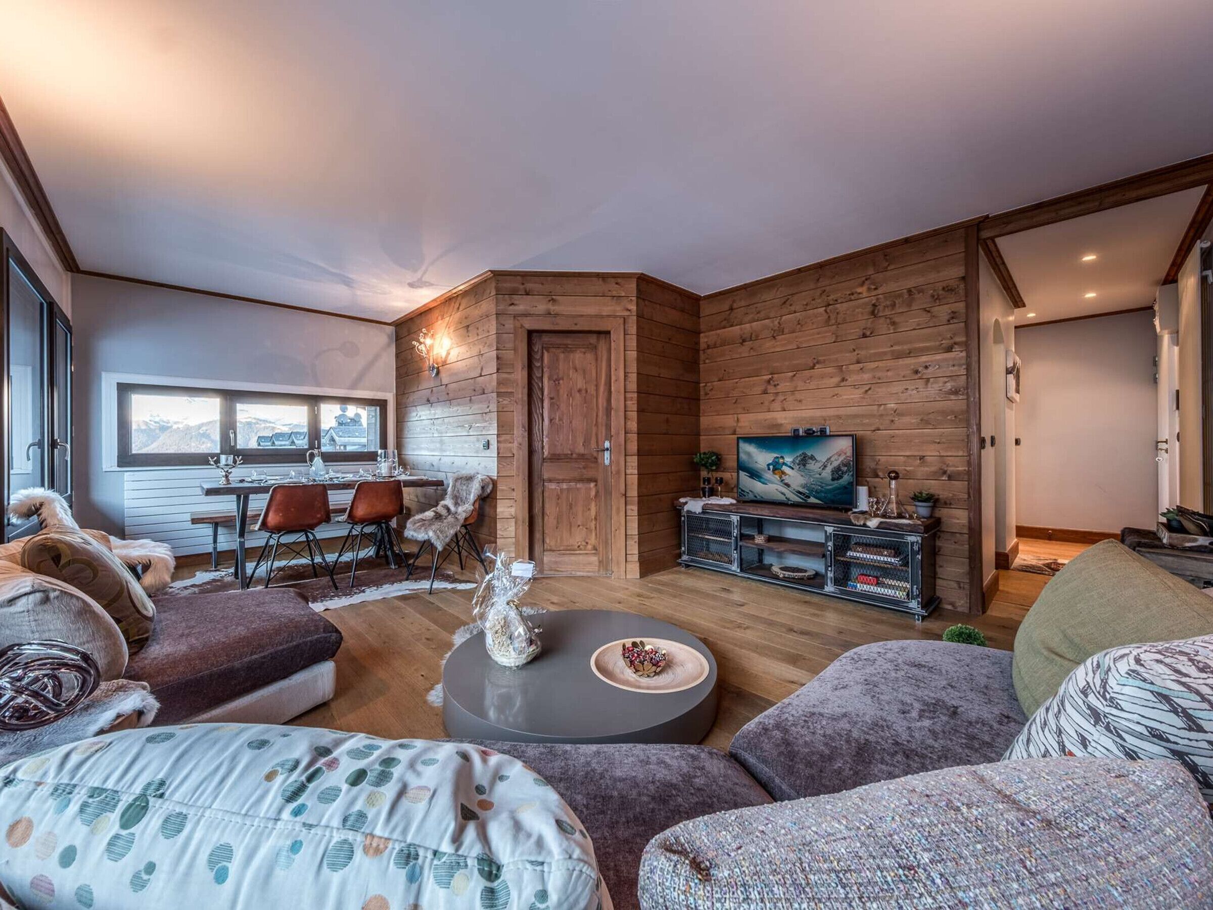 Un salon chaleureux avec un coin repas, des murs en bois, un téléviseur et une vue sur les montagnes.