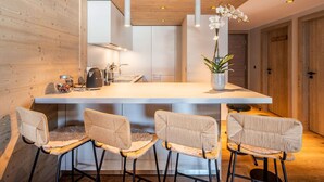 A modern kitchen with wooden walls, a central island, bar stools, and pendant lighting. - Cozy apartment, center station - 4 guests (Courchevel 1550)