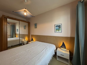 Ein Schlafzimmer mit Bett, Nachttischen, einem Spiegel und einer Deckenleuchte.