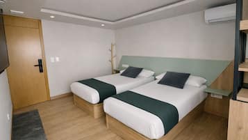 Een tweepersoonskamer met twee bedden, een houten vloer, een deur en een airconditioner.