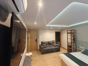 A modern hotel room with a bed, a sofa, a small table, a coat rack, and a wardrobe.
