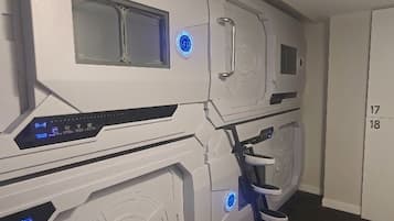 A room with a large, white, futuristic-looking machine with a control panel and a small window. There is a door with the numbers '17' and '18' on it.